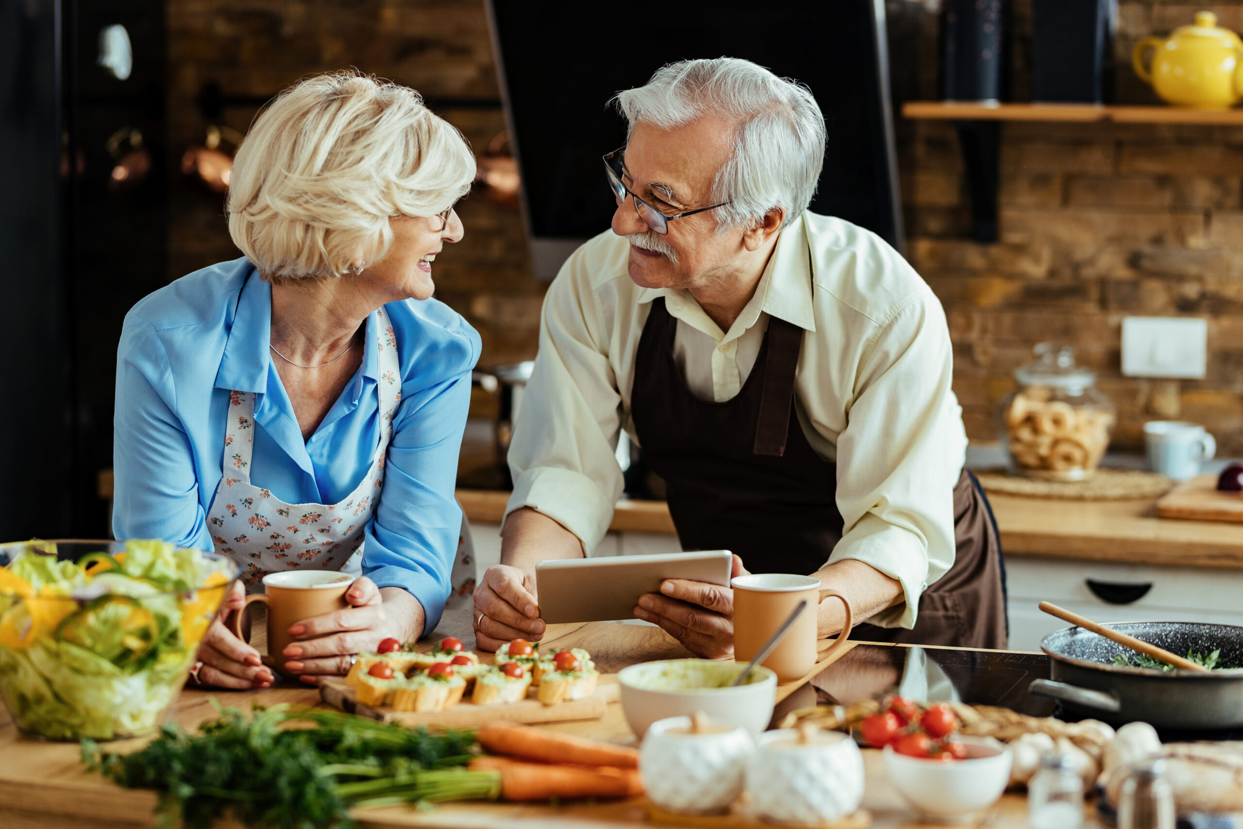 Happy senior couple communicating while preparing food and using